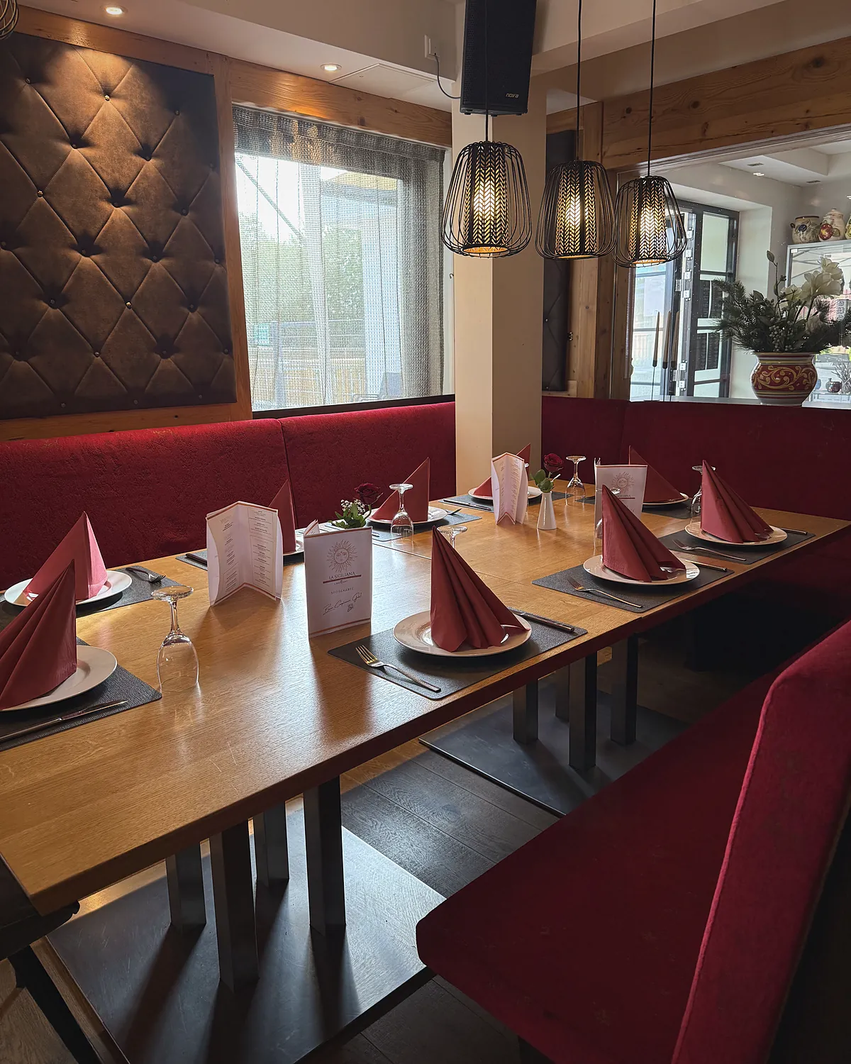 Restaurant mit roten Polsterbänken, gedeckten Holztischen und Pendelleuchten