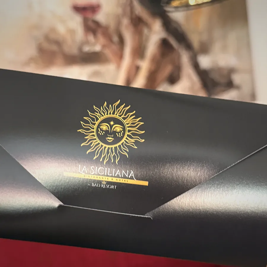 Schwarze Speisekarte mit goldener Sonne und dem Schriftzug La Siciliana