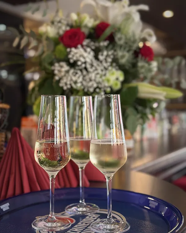 Drei Gläser Prosecco vor einem Blumenstrauß
