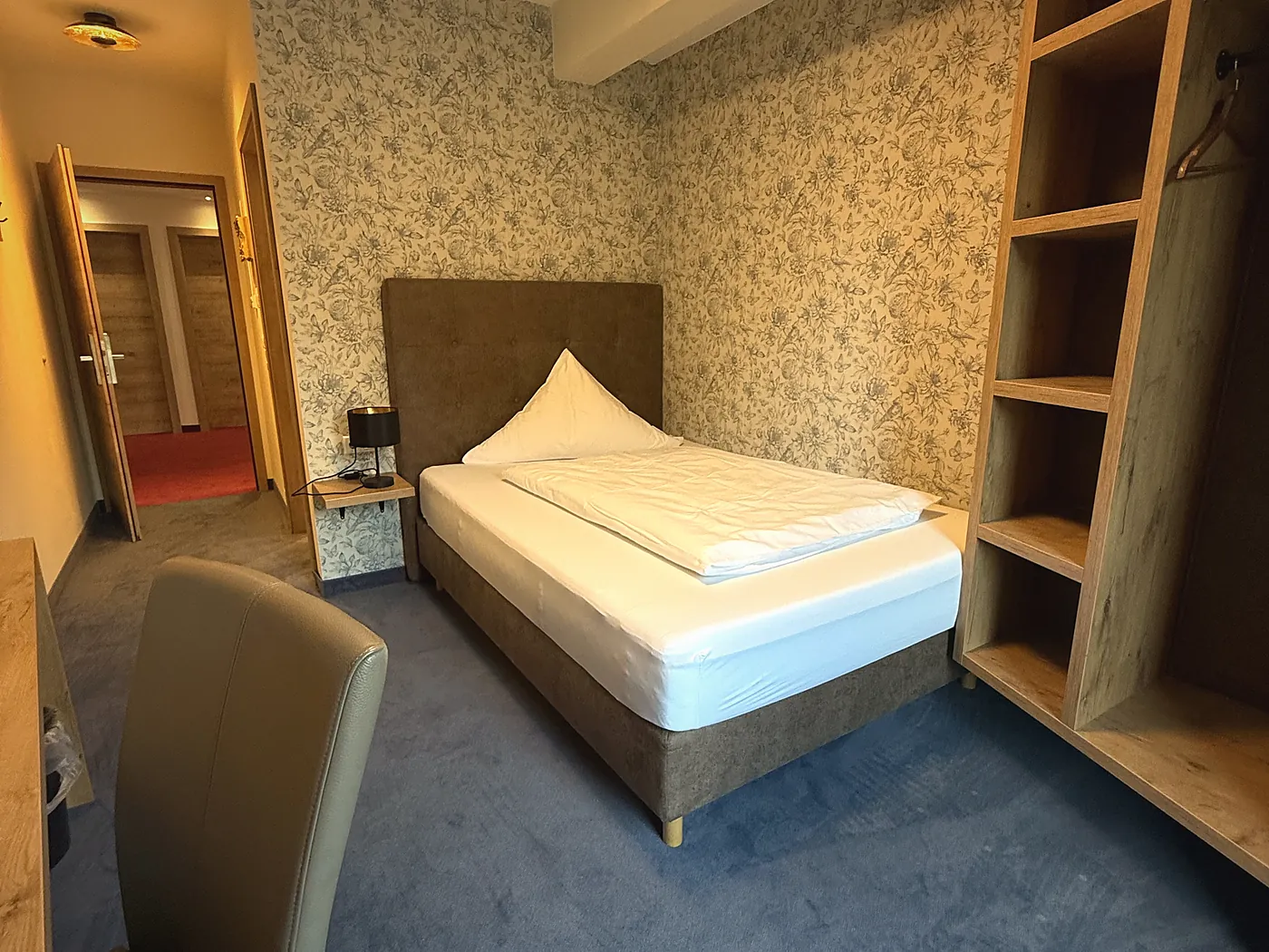 Helles Gästezimmer mit Bett, Holzregal und Tapete